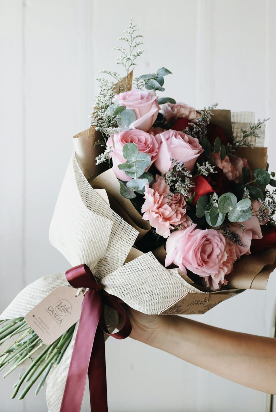 Hand holding a flower bouquet wrapped in paper and burlap.