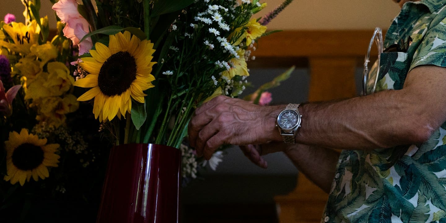 Person arranging sunflowers and gladioli in a maroon vase.
