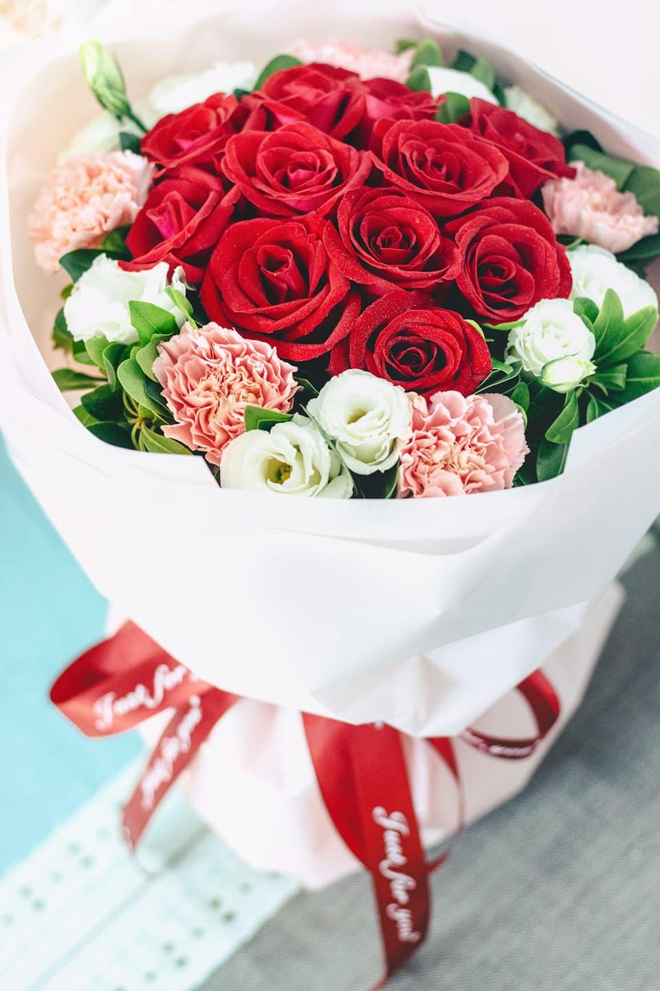 A bouquet of roses and carnations wrapped in white paper.