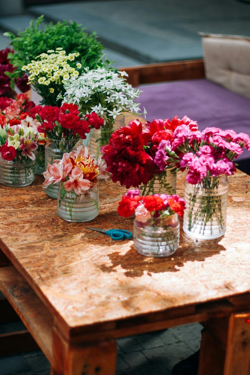 Fresh flower bouquets in glass vases on a wooden table with scissors.