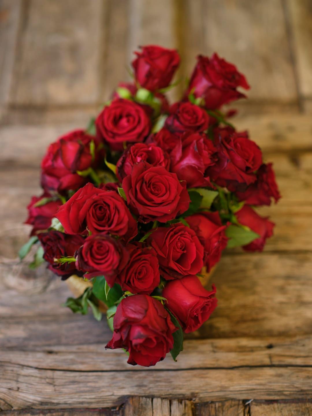 Deep red roses arranged on a rustic wooden table.